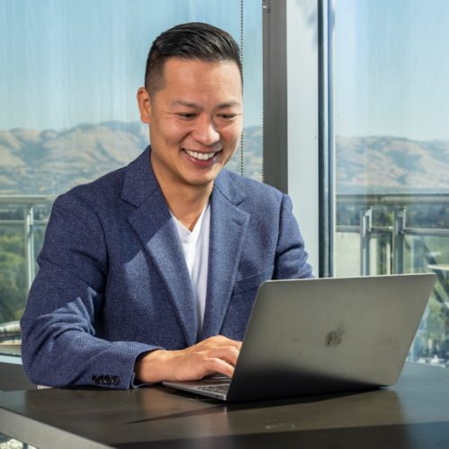 Headshot of Jason Wang. Short black hair, blue blazer. Typing on a laptop.