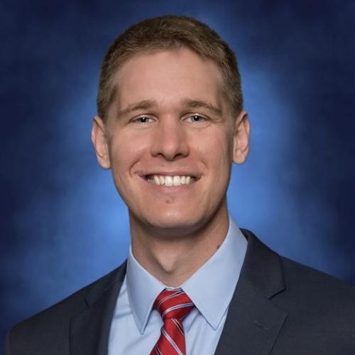 White man smiling with blonde hair and red tie