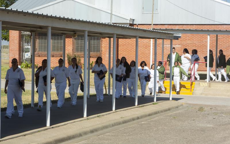 Photo of a women incarcerated walking in a single file line outdoors. 