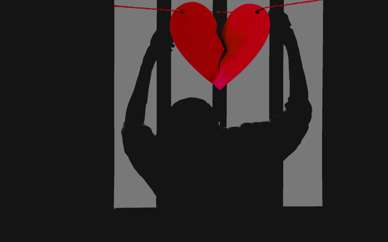 Image of a person holding prison bars with a paper broken heart hanging over them.